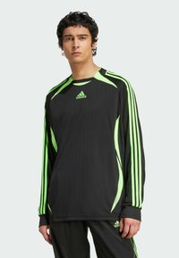 Camiseta deportiva de manga larga negra con detalles verdes, que presenta franjas en los hombros y las mangas, textura acanalada y el logo de Adidas en el pecho.