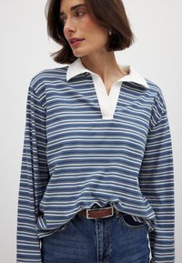 Polo a maniche lunghe a righe in blu e bianco, con colletto bianco e design a scollo a V, abbinato a jeans in denim a vita alta.