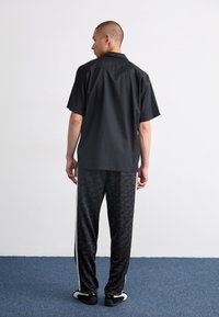 Sort kortærmet skjorte med løs pasform, parret med sorte mønstrede sweatpants med hvide sidelommer og let fodtøj.