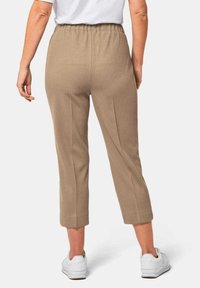 Beige verkorte broek met een geribbelde textuur en een elastische tailleband, gecombineerd met witte sportschoenen.