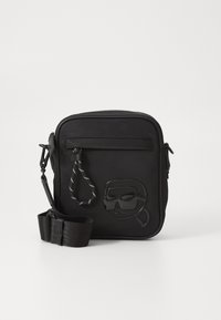 Black crossbody bag made of textured material, featuring a front pocket and embossed design of a face wearing sunglasses. Adjustable strap included.