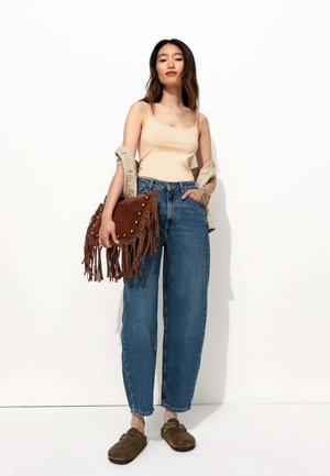 Débardeur beige, jean bleu taille haute, sac à main en cuir frangé marron avec clous, et sabots marron. Ensemble simple et décontracté sur fond blanc.