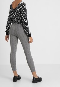 Black and white zigzag patterned top with a V-neck and long sleeves, paired with gray plaid leggings and black shoes.