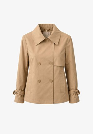 Giacca doppiopetto beige con ampio colletto, chiusura con bottoni, tasche e polsini annodati sulle maniche lunghe su sfondo bianco.