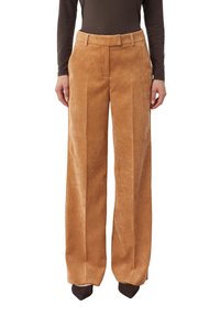 Kobieta ubrana w wysokie, szerokie spodnie z sztruksu w kolorze camel, połączone z ciemnobrązowymi spiczastymi butami i ciemną bluzką z długim rękawem.