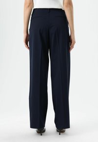 Pantalon large bleu marine à la texture lisse, doté d'une taille haute, de deux poches arrière et d'une coupe ajustée. Convient pour des tenues formelles.