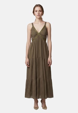 Woman standing facing forward wearing a sleeveless olive green maxi dress with a V-neck and tiered skirt, paired with golden high-heeled shoes.