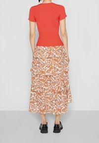Top rosso a righe con maniche corte abbinato a una gonna maxi a balze con motivo floreale in arancione e crema, indossato con scarpe chunky nere.