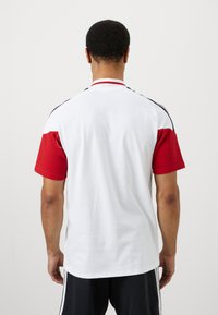 Rød og hvit polo med korte ermer som har en ribbede krage, teksturerte røde ermer og svarte sidelister. Glatt stoff med en avslappet passform.