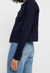 Giacca di jeans blu navy con un design aderente, chiusura a bottoni e due tasche sul petto. Presenta una texture solida e un classico stile colletto.