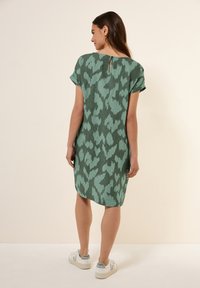 Vihreä kuviollinen mekko lyhyillä hihoilla, avainaukko takana ja suora leikkaus, yhdistettynä valkoisiin lenkkareihin.