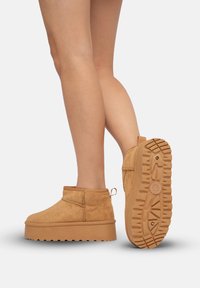 Botas de tobillo de ante color marrón con suela de plataforma gruesa y suela de goma texturizada, que incluyen una lengüeta y detalles de costura mínimos.