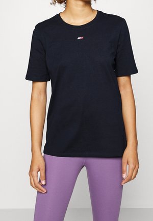 Camiseta de manga corta de color azul marino en algodón, con cuello redondo y un pequeño logo en el pecho. Combinada con leggins de color púrpura claro.