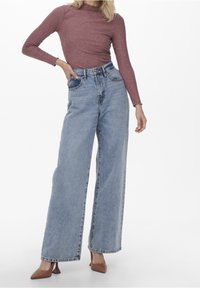 Jeans blu a vita alta e gamba larga in denim chiaro con una finitura sbiadita. Abbinati a un top fitted a maniche lunghe in maglina bordeaux e tacchi marroni.