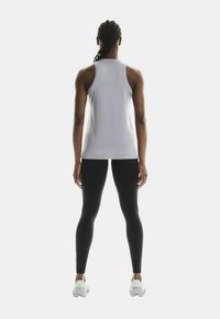 Top atletico senza maniche di colore grigio chiaro abbinato a leggings neri. Tessuto liscio e elastico con un design aderente e spalline strette.