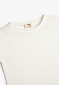 Hvid bomulds t-shirt til børn med rund hals og korte ærmer. Har et mærke, der læser "Koton Kids", syet ind i halsudskæringen.
