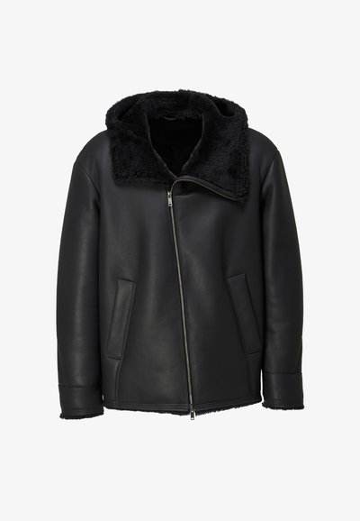 Schwarze Lederjacke mit diagonalem silbernem Reißverschluss, zwei Fronttaschen und einem samtigen, mit schwarzem Fell gefütterten Kragen und Bündchen.
