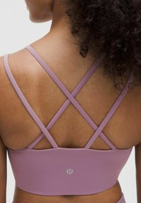 Reggiseno sportivo di un delicato colore viola chiaro con una superficie liscia, dotato di spalline incrociate sulla schiena e un dettaglio con logo al centro.