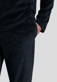 Sudadera de forro polar negra y pantalones a juego con un acabado texturizado. Incluye un bolsillo en los pantalones y puños acanalados en la parte superior para mayor comodidad.