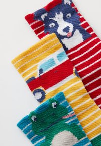 Drei Paar Socken mit verspielten Designs: ein blau-weißer Hund, ein rot-gelbes Auto und ein grüner Frosch, alle mit bunten Streifen.
