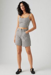 Kortärmad rutig topp och matchande shorts i svart, vitt och grått. Outfitten har tunna band och fickor på shortsen. Svarta sandaler.