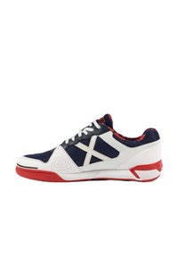 Zapatilla deportiva con parte superior de malla azul marino, acentos sintéticos blancos, suela roja y costuras blancas contrastantes en un diseño angular.