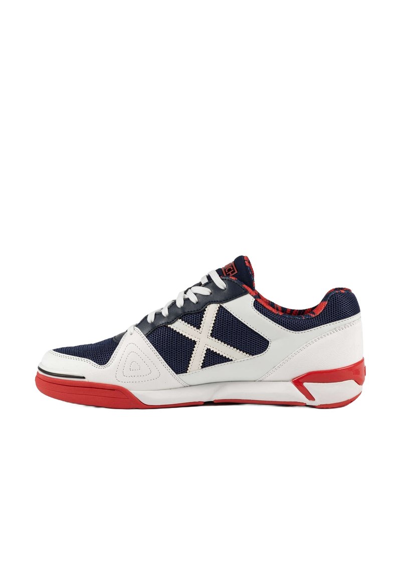 Zapatilla deportiva con parte superior de malla azul marino, acentos sintéticos blancos, suela roja y costuras blancas contrastantes en un diseño angular.