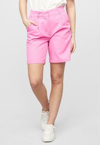 Pantaloni corti rosa con un design su misura, caratterizzati da pieghe frontali e tasche laterali. Realizzati in tessuto liscio, terminano appena sopra il ginocchio.