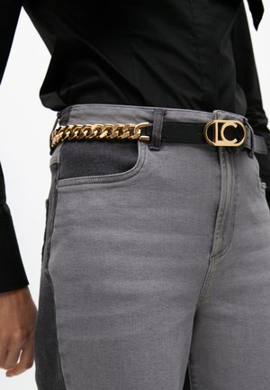 Graue Denim-Jeans mit einem schwarzen Gürtel, der über ein goldenes Kettendetail und eine runde Schnalle verfügt. Weiche Textur mit seitlich sichtbaren Taschen.