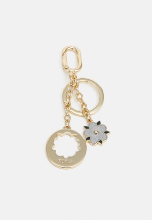 Gold keychain featuring a circular cutout tag inscribed with "Furla," and a textured gray flower charm with green accents attached by a chain.