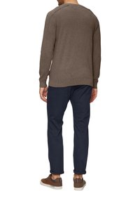 Bruine gebreide trui met geribbelde manchetten en zoom, gecombineerd met navy broek. Schoenen zijn bruin met accenten, in een casual ontwerp.