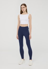 Leggings navy con una vita alta e strisce laterali abbinati a un crop top bianco aderente. Texture liscia, vestibilità su misura e design moderno.