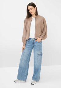 Brown bomber jacket with a soft texture, paired with light blue wide-leg jeans featuring cargo pockets and a white t-shirt underneath.