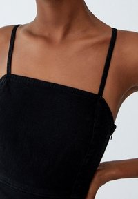 Svart denimtopp med tunna axelband, fyrkantig halsringning och en figursydd silhuett. Har subtila sömmar och ett strukturerat tyg.