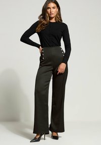 Hoge taille zwarte broeken met gouden knopen aan de zijkant, gecombineerd met een aansluitende zwarte cardigan met lange mouwen. Glad stof, wijde pijpen ontwerp.