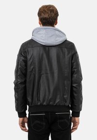 Schwarze Leder-Bomberjacke mit einem grauen Hoodie darunter, gerippte Bündchen und Saum; glatte Textur mit minimal sichtbaren Hardwaredetails.