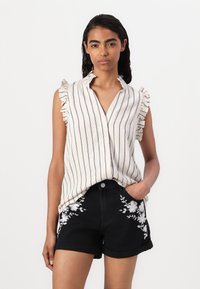 Chemisier sans manches rayé avec un col volanté en crème et bleu marine. Associé à un short noir avec une broderie florale blanche sur les poches.