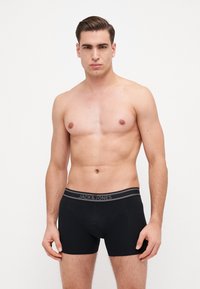 Boxer in nero con elastico grigio che presenta il logo "JACK & JONES", realizzati in un materiale liscio e elasticizzato. Design semplice e aderente.