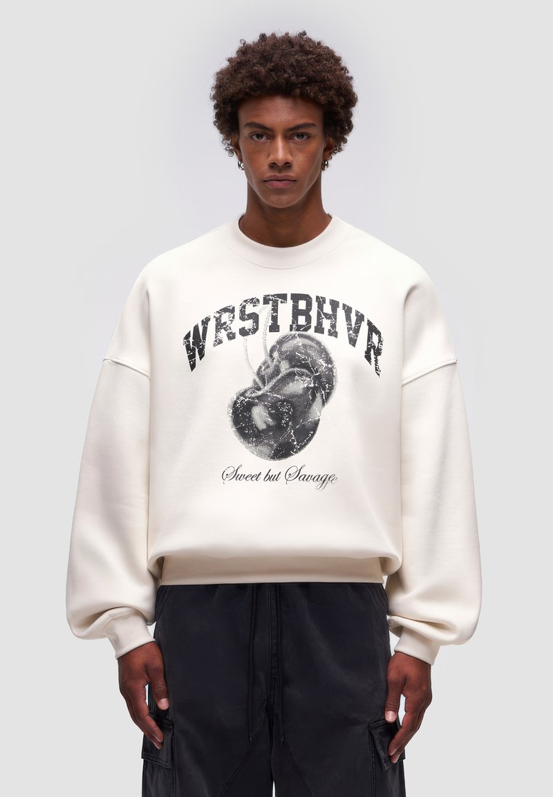 Felpa color crema con vestibilità oversize, colletto rotondo e stampa grafica che presenta "WRSTBVR" e un design a forma di cuore con la scritta "Sweet but Savage."