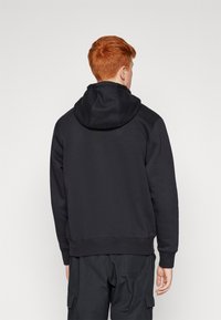 Sudadera negra con un interior suave y texturizado, que presenta una gran capucha, puños acanalados y un dobladillo recto. Diseño sencillo sin logotipos ni patrones.
