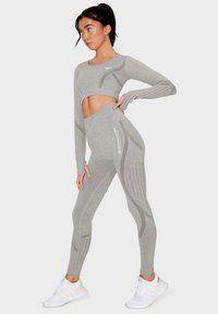 Gray cropped long-sleeve top and high-waisted leggings with cut-out detailing and stripe patterns, paired with white athletic shoes.