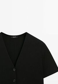 Cardigan noir à manches courtes en V avec deux boutons sur le devant et une étiquette de marque visible au niveau du col.
