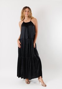 Abito lungo nero realizzato in tessuto morbido con un design a strati, spalline sottili e una silhouette fluente.