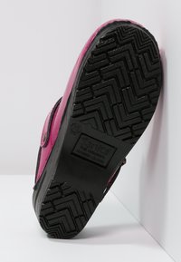 Rosa träskor med en glänsande finish, som har en robust svart gummisula med ett zigzagmönster och en märkeslogotyp på undersidan.