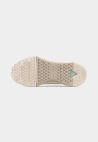 Εξωτερική σόλα μπεζ αθλητικού παπουτσιού με τριγωνικά σχέδια πέλματος, δύο οριζόντιες αυλακώσεις και ένα μικρό διαφανές τρίγωνο κοντά στη φτέρνα.