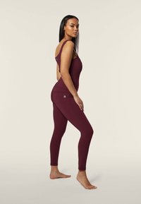 Body in athleisure color bordeaux con design a schiena scoperta e spalline larghe, abbinato a leggings aderenti coordinati; texture liscia con un sottile dettaglio di branding.