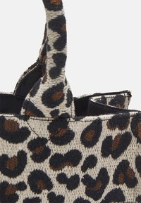 Canvas tas met luipaardprint, voorzien van zwarte en bruine vlekken op een beige achtergrond. Heeft bovenhandvatten en een open interieur.