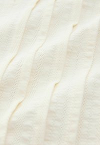 Tissu tricoté de couleur crème avec un motif texturé, comprenant des rayures verticales et de petits trous pour la respirabilité. Matériau doux et léger.