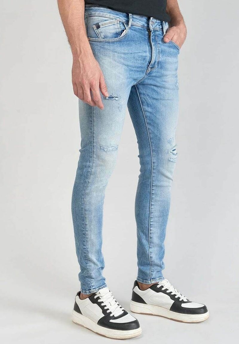 Vaaleansiniset kapeat farkut, joissa on kulutettuja yksityiskohtia, haalistunut pinta ja klassinen viisi taskua -kuvio. Yhdistetty mustavalkoisiin lenkkareihin.