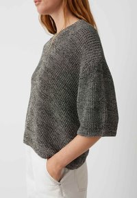 Grauer Kurzarm-Pullover aus Strick mit strukturiertem Muster, weit geschnittenem Ausschnitt und lockerer Passform, kombiniert mit weißen Hosen.